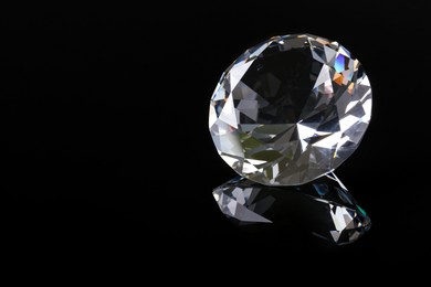 Beautiful shiny diamond on black mirror surface, closeup. Space for text