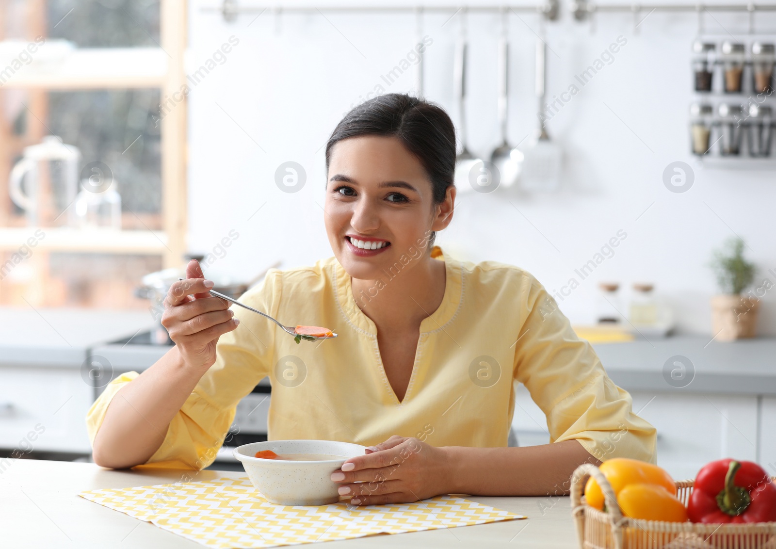 Photo of Young woman eating tasty vegetable soup at table in kitchen