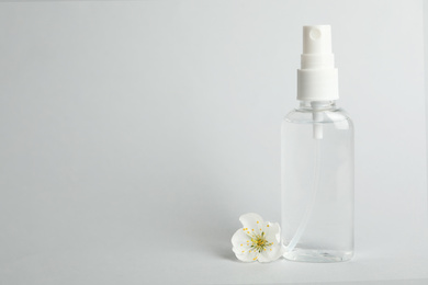 Photo of Antiseptic spray and flower on light grey background, space for text