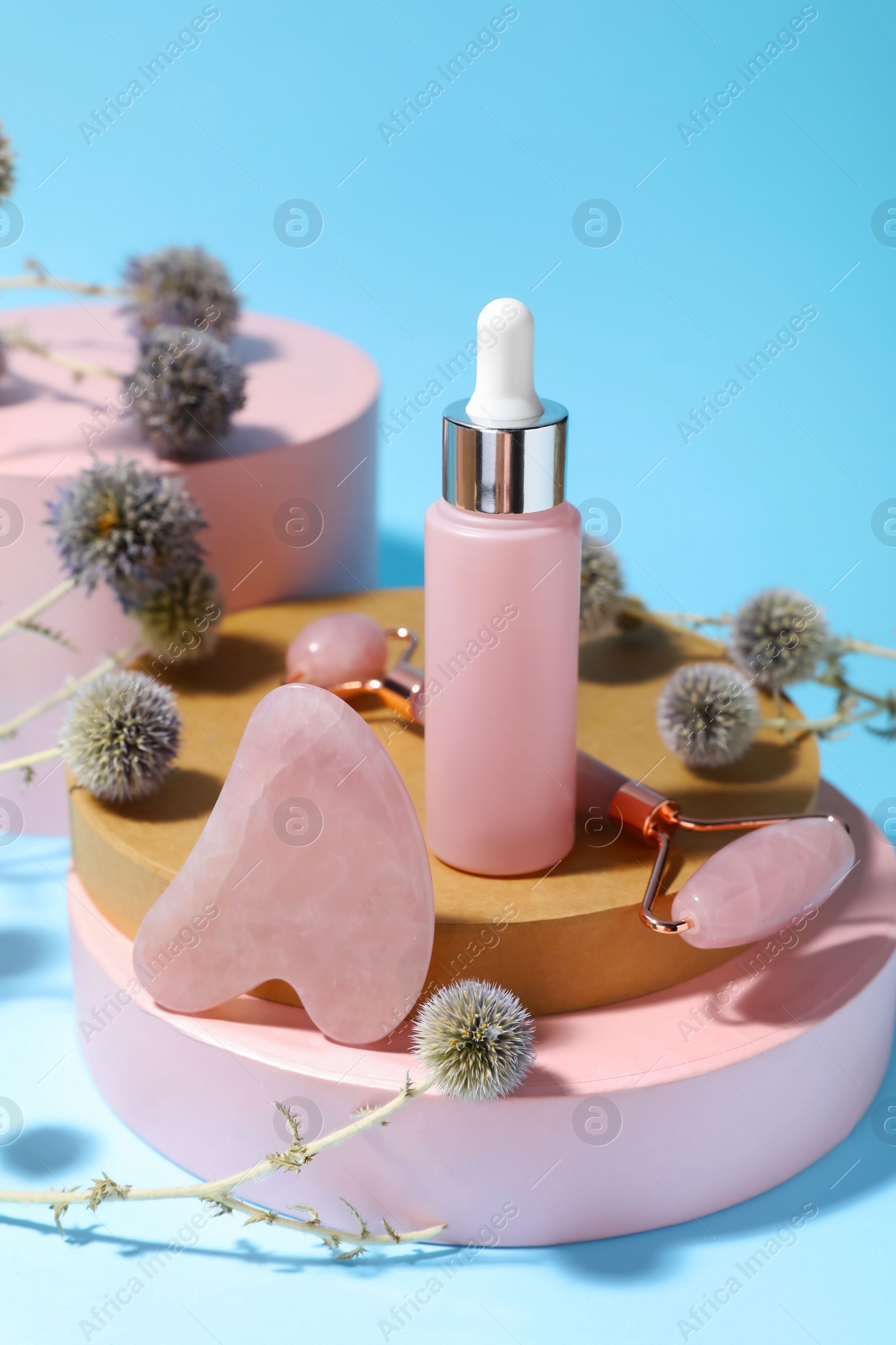 Photo of Beautiful composition with gua sha stone, face roller and bottle of serum on light blue background