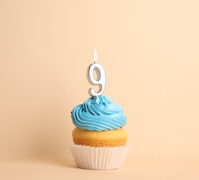 Birthday cupcake with number nine candle on beige background
