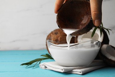 Woman pouring delicious coconut milk into bowl on light blue wooden table, closeup. Space for text