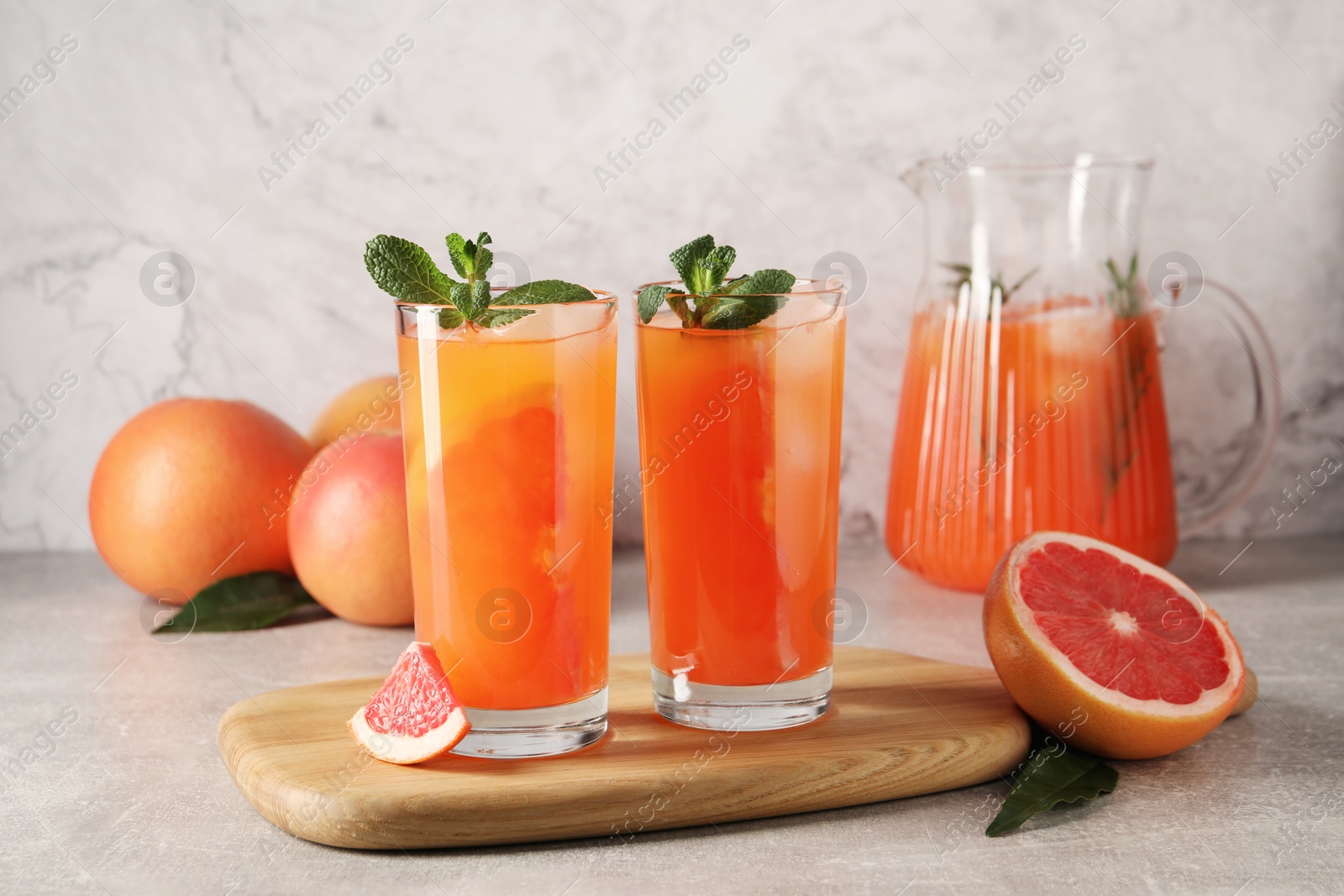 Photo of Tasty freshly made grapefruit juice, fruits and mint on light grey table