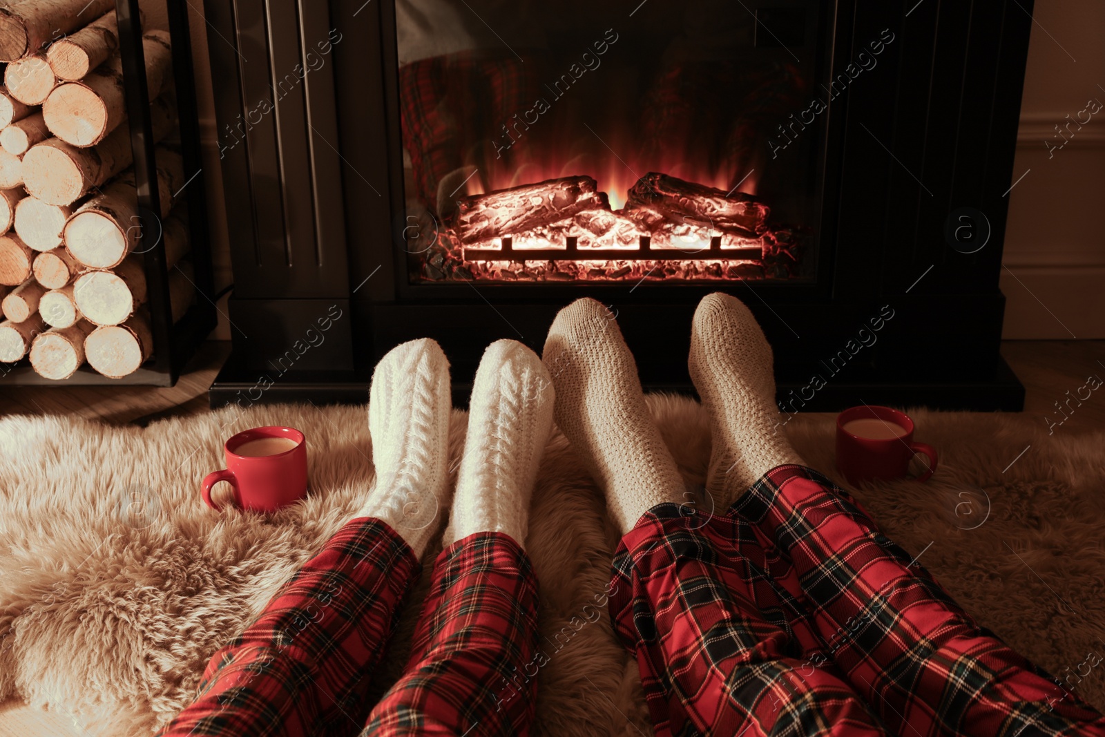 Photo of Couple in knitted socks near fireplace at home, closeup of legs