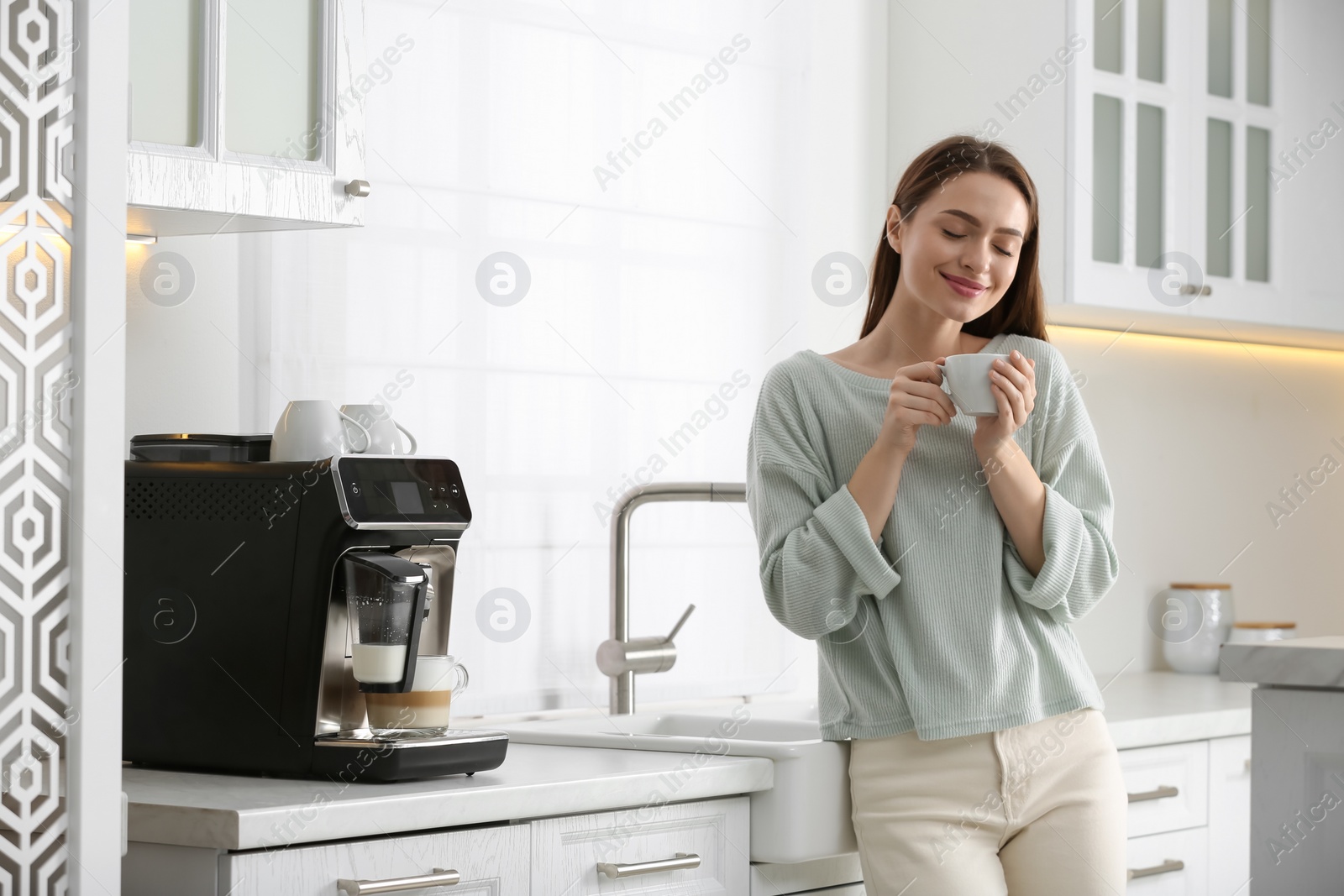 Photo of Young woman enjoying fresh aromatic coffee near modern machine in kitchen