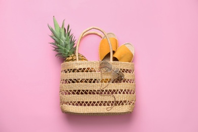 Photo of Elegant woman's straw bag with shoes, sunglasses and pineapple on pink background, top view