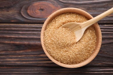 Photo of Bowl and spoon with brown sugar on wooden table, top view. Space for text