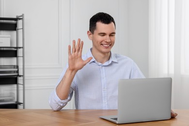Man waving hello while having video chat on laptop in office