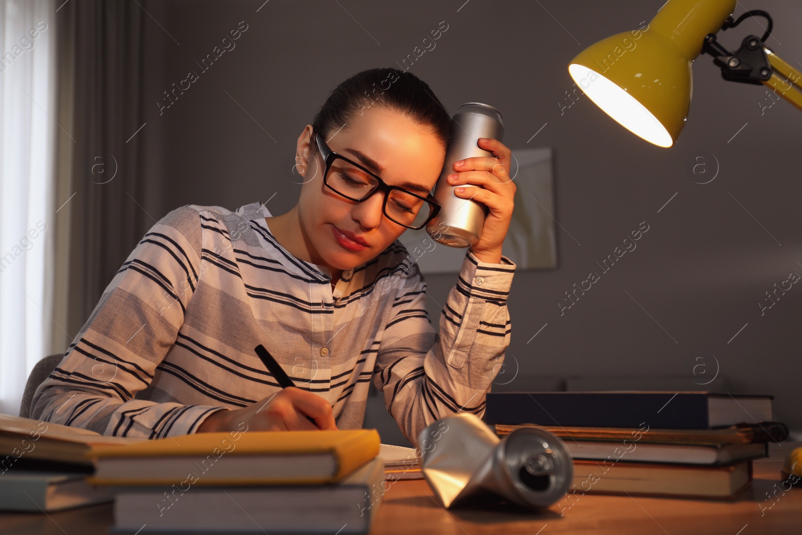 Photo of Tired young woman with energy drink studying at home