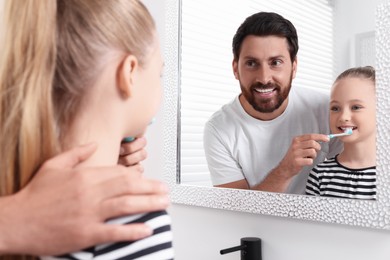 Photo of Father helping his daughter to brush teeth near mirror in bathroom