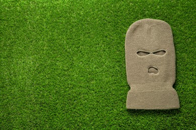 Beige knitted balaclava on green grass, top view. Space for text