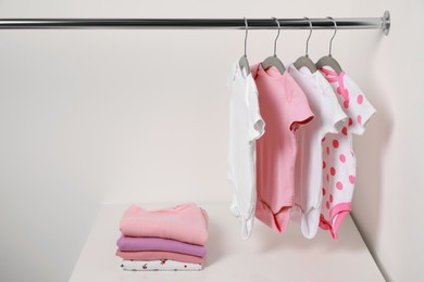 Photo of Hangers with baby bodysuits and stack of clothes near white wall. Space for text