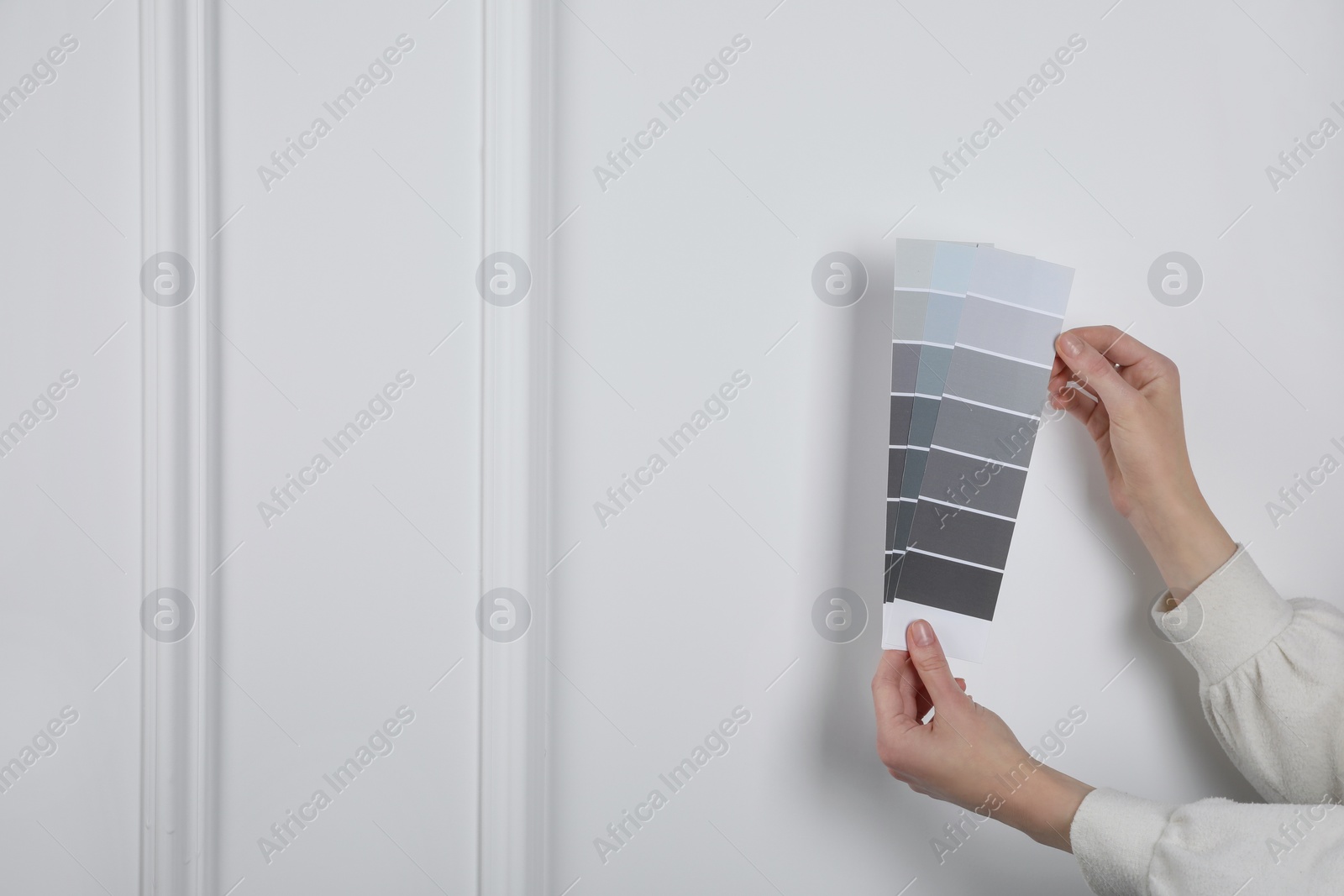 Photo of Woman with paint chips choosing color near white wall, closeup. Interior design