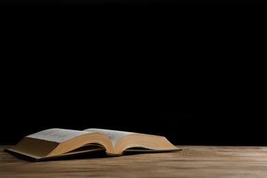 Photo of Open Bible on wooden table against black background, space for text. Christian religious book