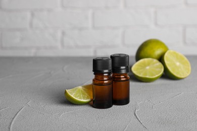Bottles of essential oil with limes on grey table, closeup