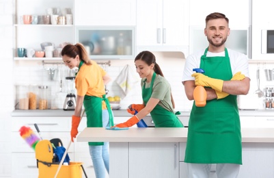 Photo of Team of professional janitors in uniform cleaning kitchen