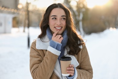 Portrait of smiling woman with paper cup of coffee in snowy park