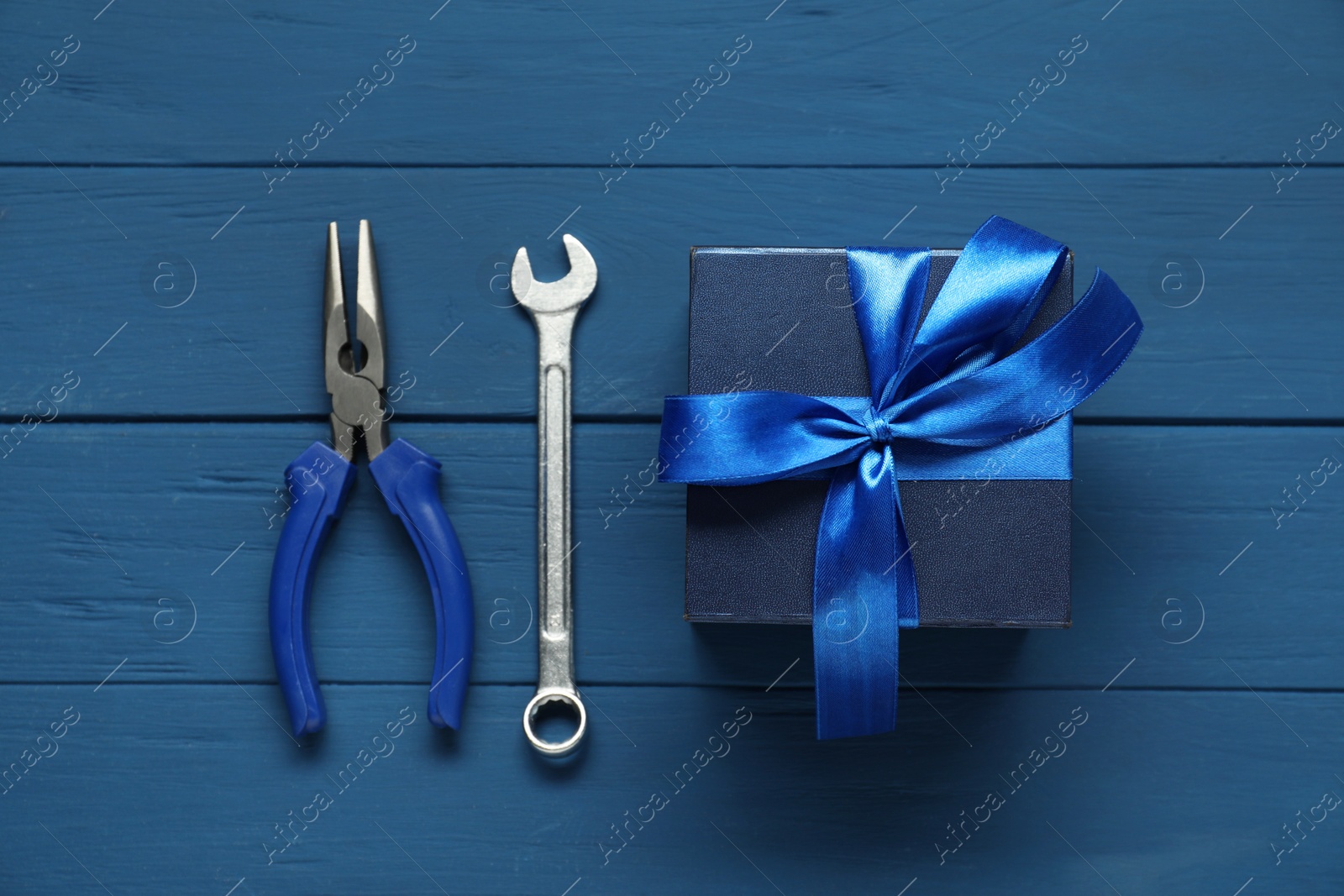 Photo of Father's day celebration. Gift box, pliers and wrench on blue wooden table, top view