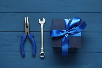 Father's day celebration. Gift box, pliers and wrench on blue wooden table, top view