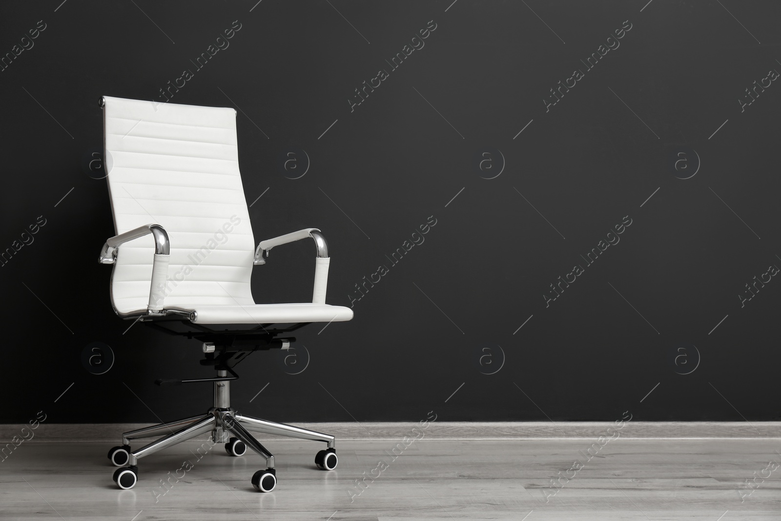 Photo of Comfortable office chair near black wall indoors. Space for text