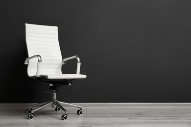 Photo of Comfortable office chair near black wall indoors. Space for text