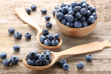 Photo of Spoons and bowl with tasty fresh blueberries on wooden table