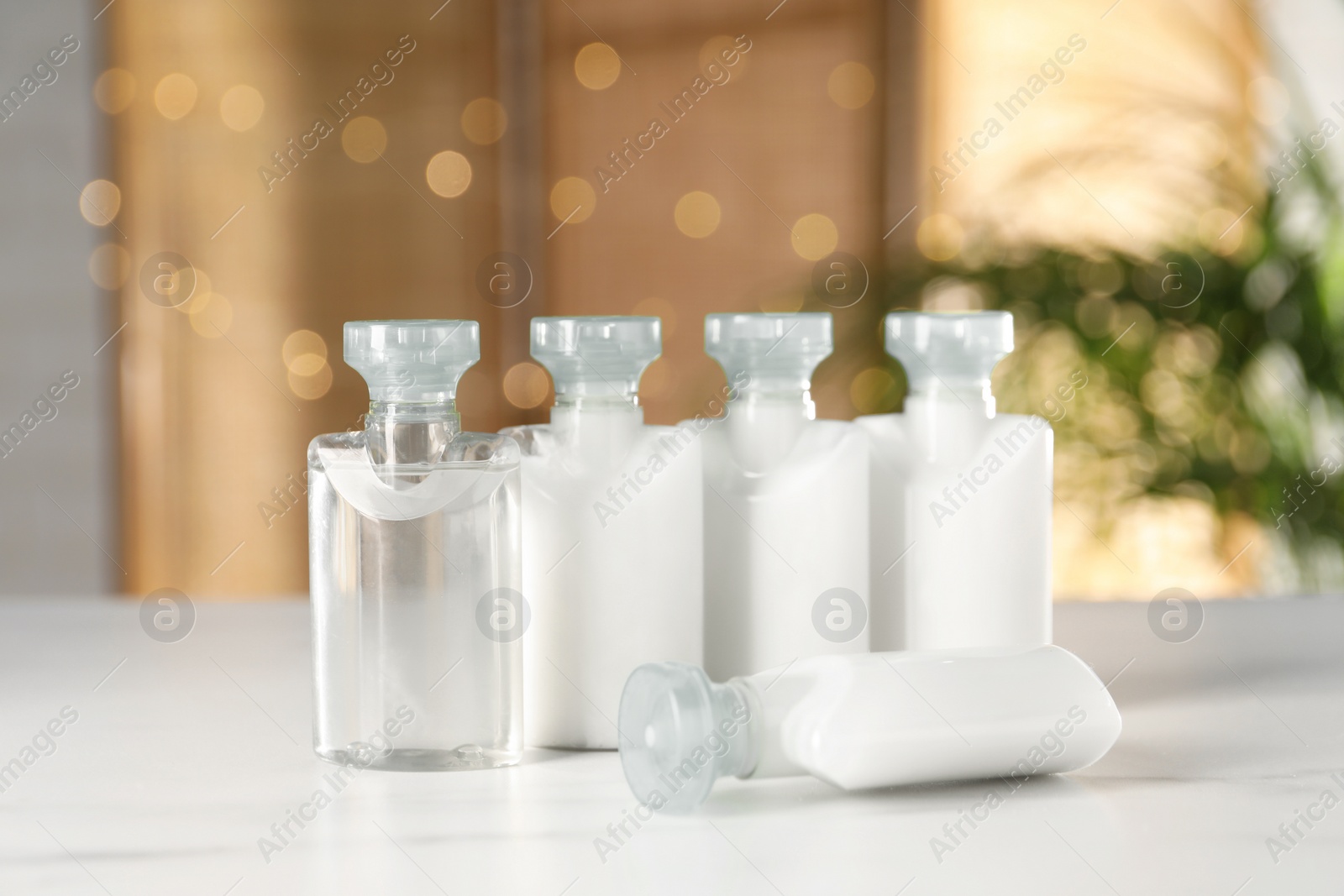 Photo of Mini bottles of cosmetic products on white table against blurred background