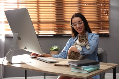 Photo of Young woman with cat working on computer at table. Home office concept