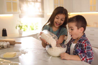 Cute little children cooking dough in kitchen at home