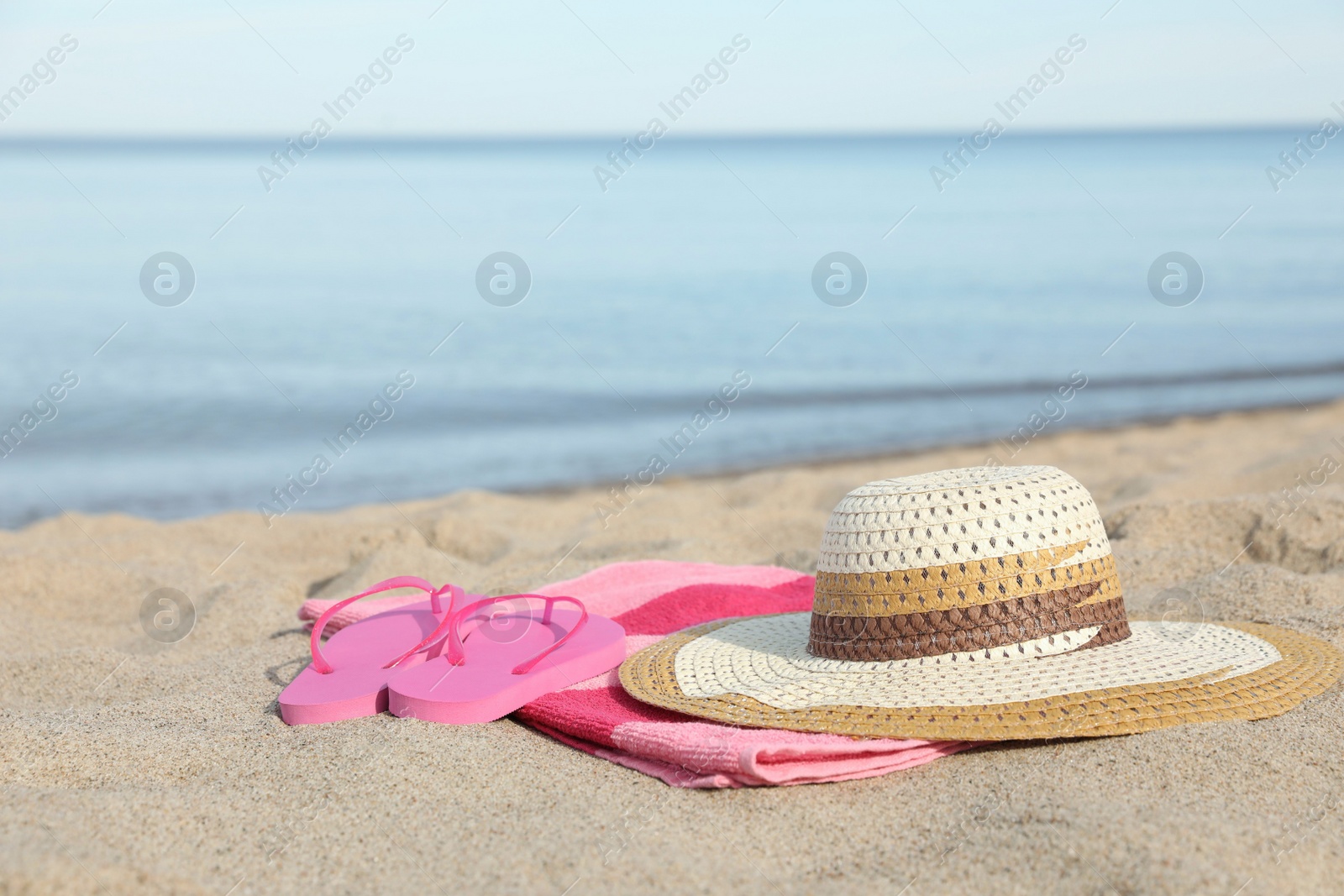 Photo of Beach towel with straw hat and slippers on sand near sea