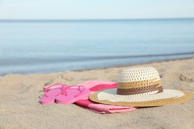 Beach towel with straw hat and slippers on sand near sea