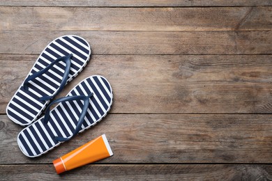 Stylish flip flops and sun protection product on wooden background, flat lay. Space for text