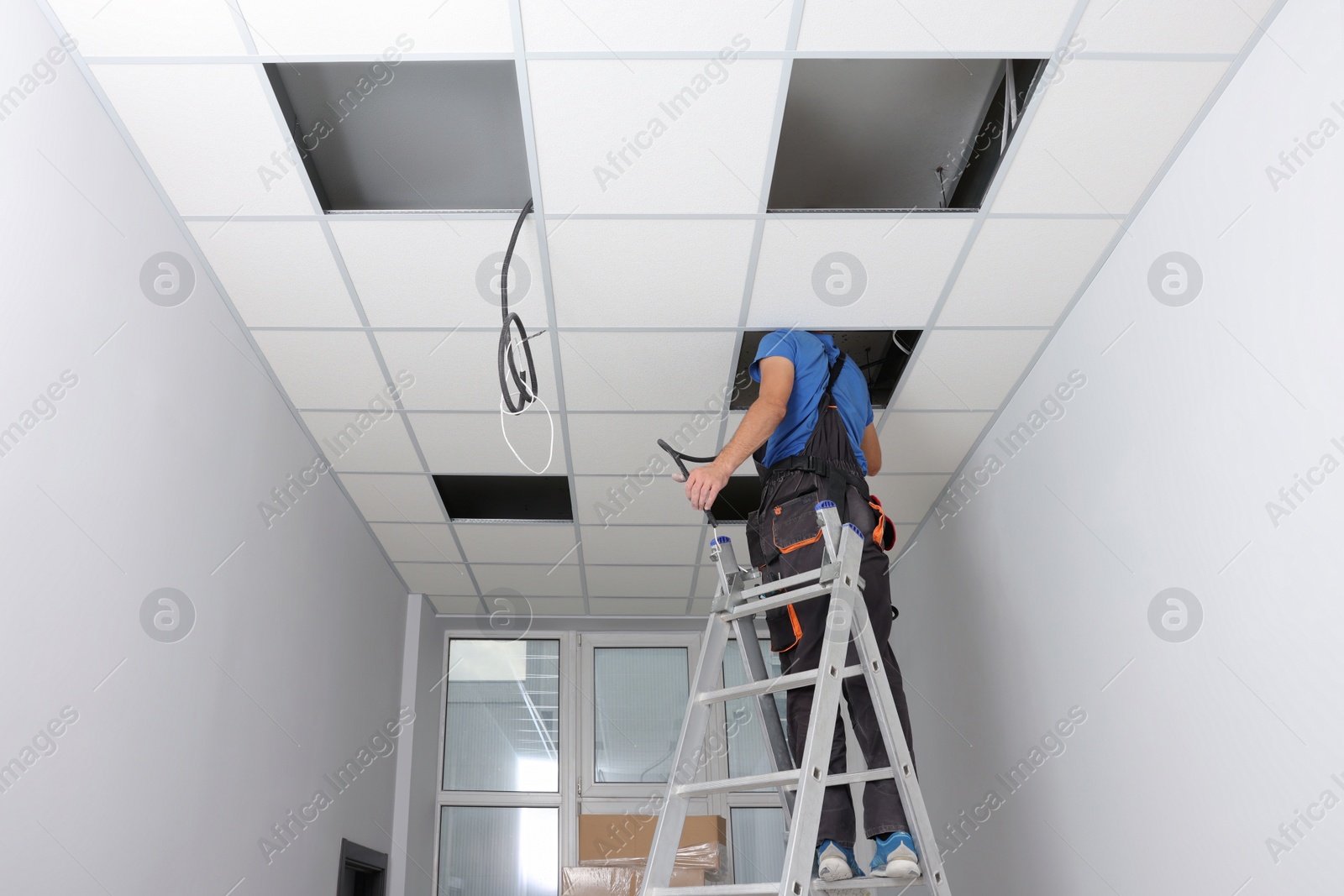 Photo of Installing ceiling lighting. Electrician working on step ladder in room