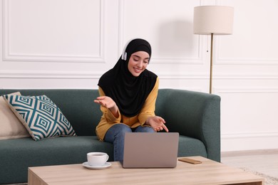 Muslim woman in hijab using video chat on laptop in room