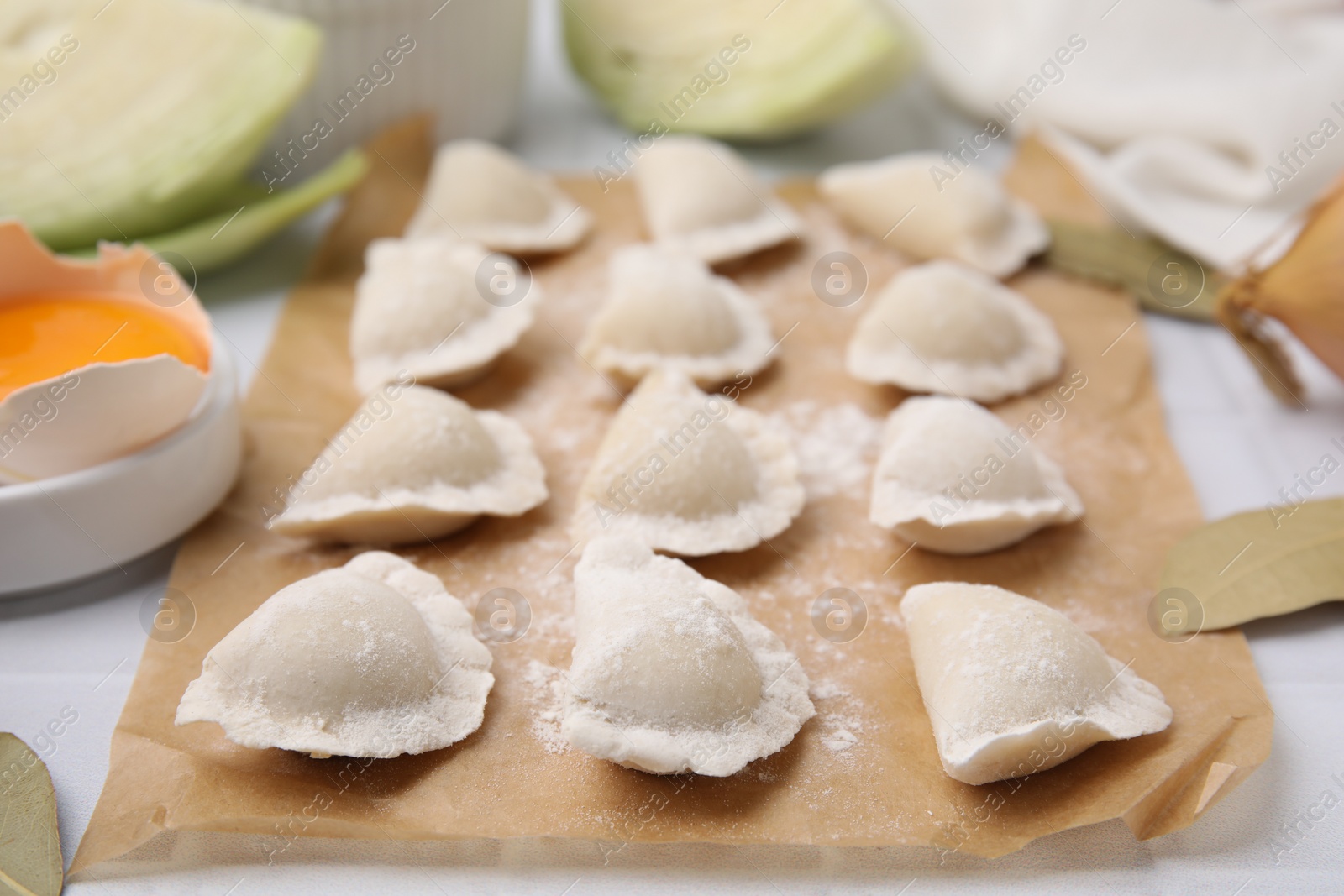 Photo of Raw dumplings (varenyky) with tasty filling and flour on parchment paper, closeup