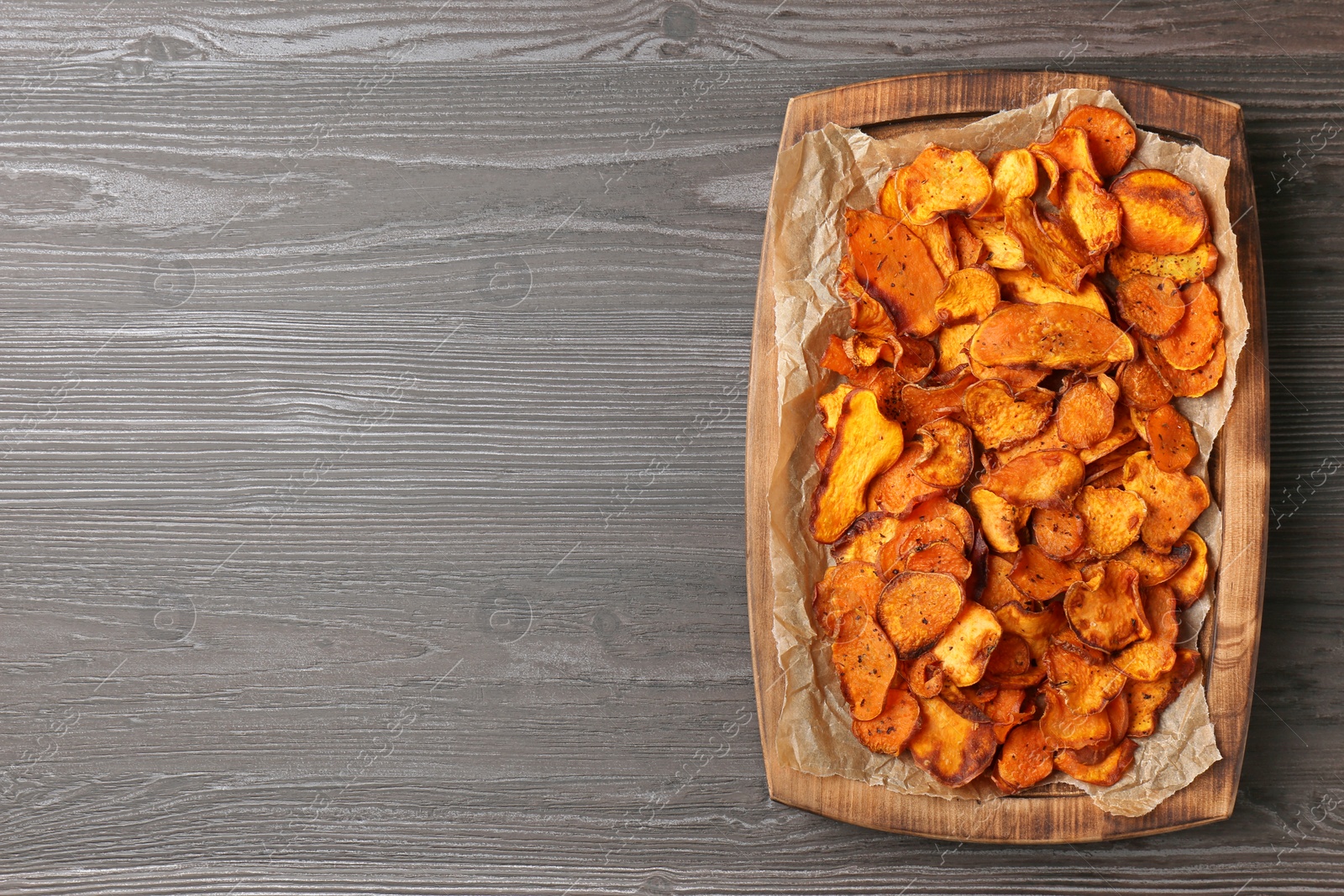 Photo of Tray with sweet potato chips on wooden table, top view. Space for text