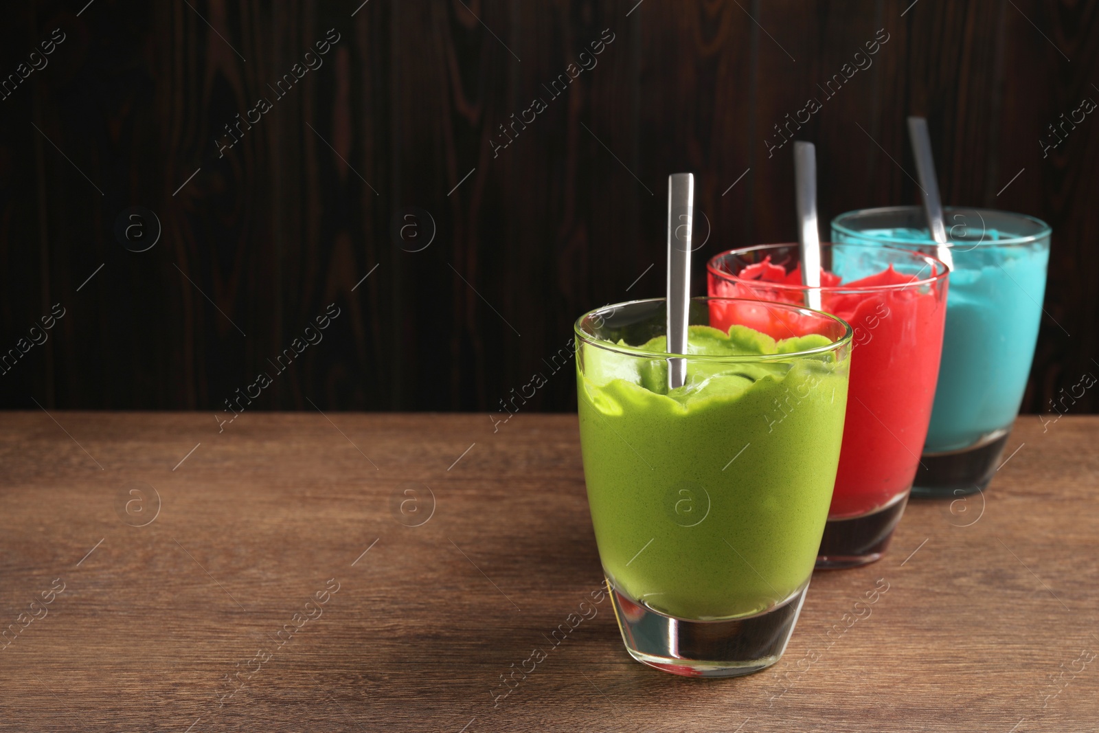 Photo of Glasses of different cream with food coloring on wooden table, space for text