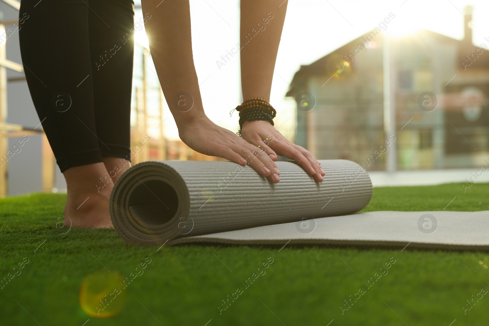 Photo of Young woman rolling yoga mat in sunlit room, closeup