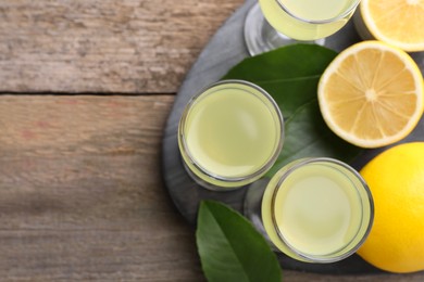 Tasty limoncello liqueur, lemons and green leaves on wooden table, top view. Space for text