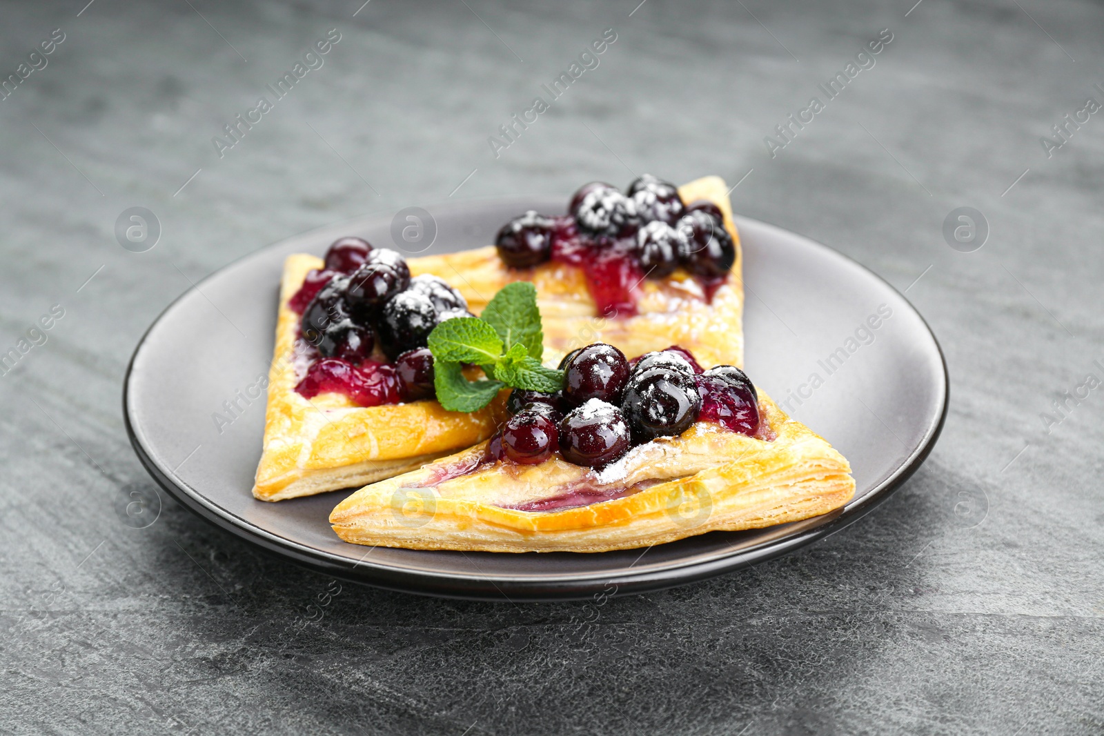 Photo of Fresh tasty puff pastry with sugar powder, jam, sweet berries and mint on grey table