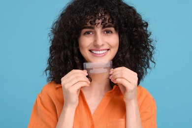Young woman holding teeth whitening strips on light blue background