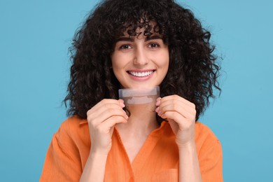 Photo of Young woman holding teeth whitening strips on light blue background