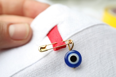 Woman holding clothing with evil eye safety pin, closeup