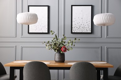 Photo of Soft chairs, table and vase with plants in stylish dining room