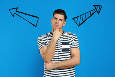 Image of Pensive man standing near blue wall with arrows