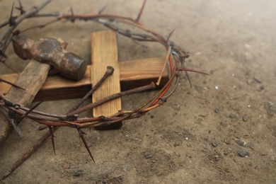 Photo of Crown of thorns, wooden cross and hammer with nails on ground, space for text. Easter attributes