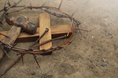 Crown of thorns, wooden cross and hammer with nails on ground, space for text. Easter attributes