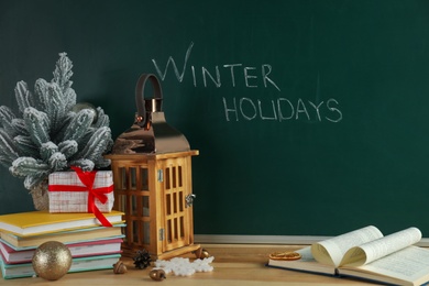 Text Winter Holidays on chalkboard near wooden table with Christmas decor and books