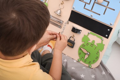 Photo of Little boy playing with busy board on bed