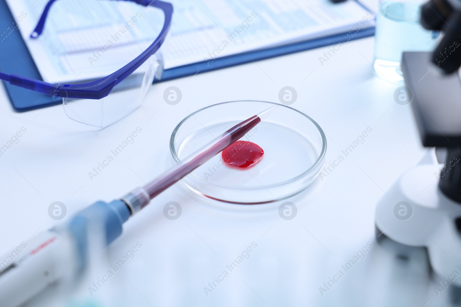 Photo of Dripping blood sample onto Petri dish on white table in laboratory, closeup